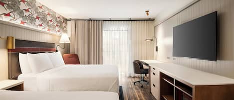 Une chambre d’hôtel avec deux lits, un bureau, une chaise, une télévision et une grande fenêtre avec des rideaux.