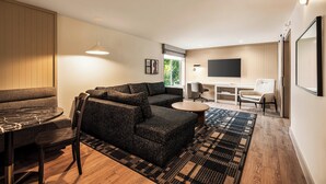 A modern living room with a sectional sofa, a dining table, and a TV mounted on the wall. - Holiday Inn Downtown - Missoula by IHG (Missoula)