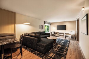 A modern living room with a sectional sofa, a dining table, and a TV mounted on the wall.