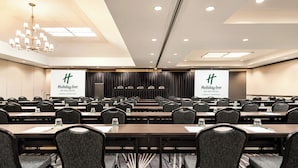 A conference room with multiple tables and chairs, a chandelier, and banners for Holiday Inn An Iho Hotel in Missoula Downtown. - Holiday Inn Downtown - Missoula by IHG (Missoula)