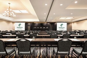 A conference room with multiple tables and chairs, a chandelier, and banners for Holiday Inn An Iho Hotel in Missoula Downtown.