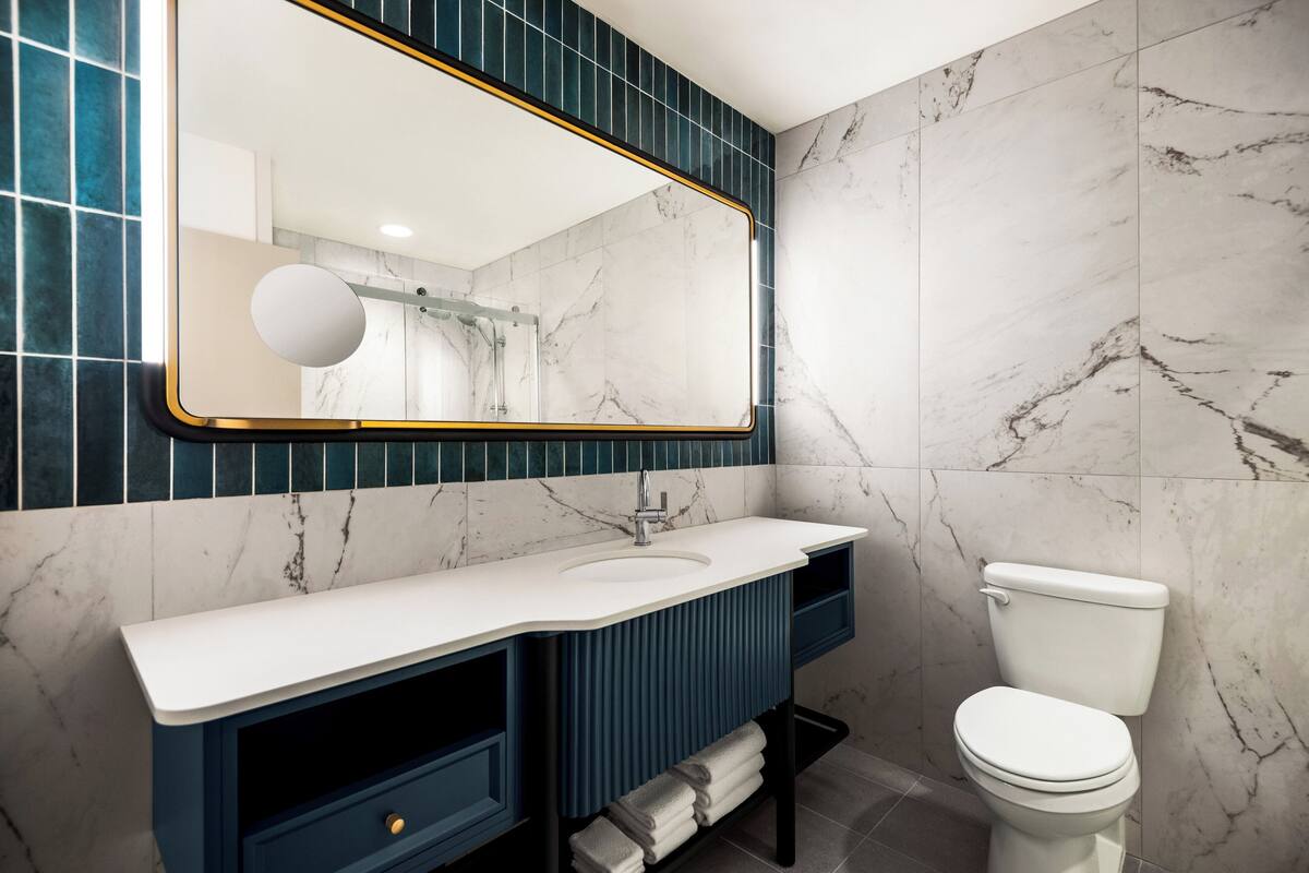 A modern bathroom with a white sink, dark blue vanity, and a white toilet.