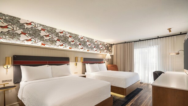 A hotel room with two beds, a desk, and a headboard with a floral design. - Holiday Inn Downtown - Missoula by IHG (Missoula)