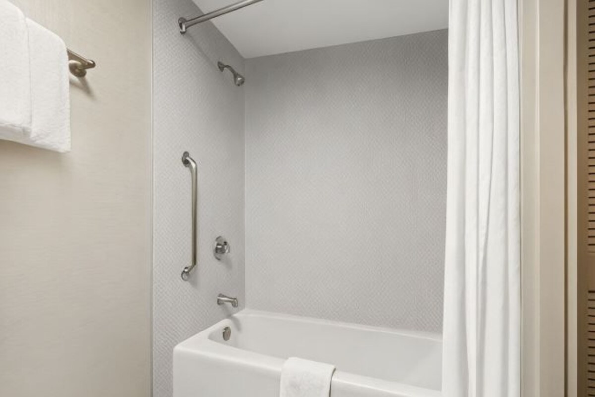 Un baño con bañera, barras de apoyo y un perchero para toallas.