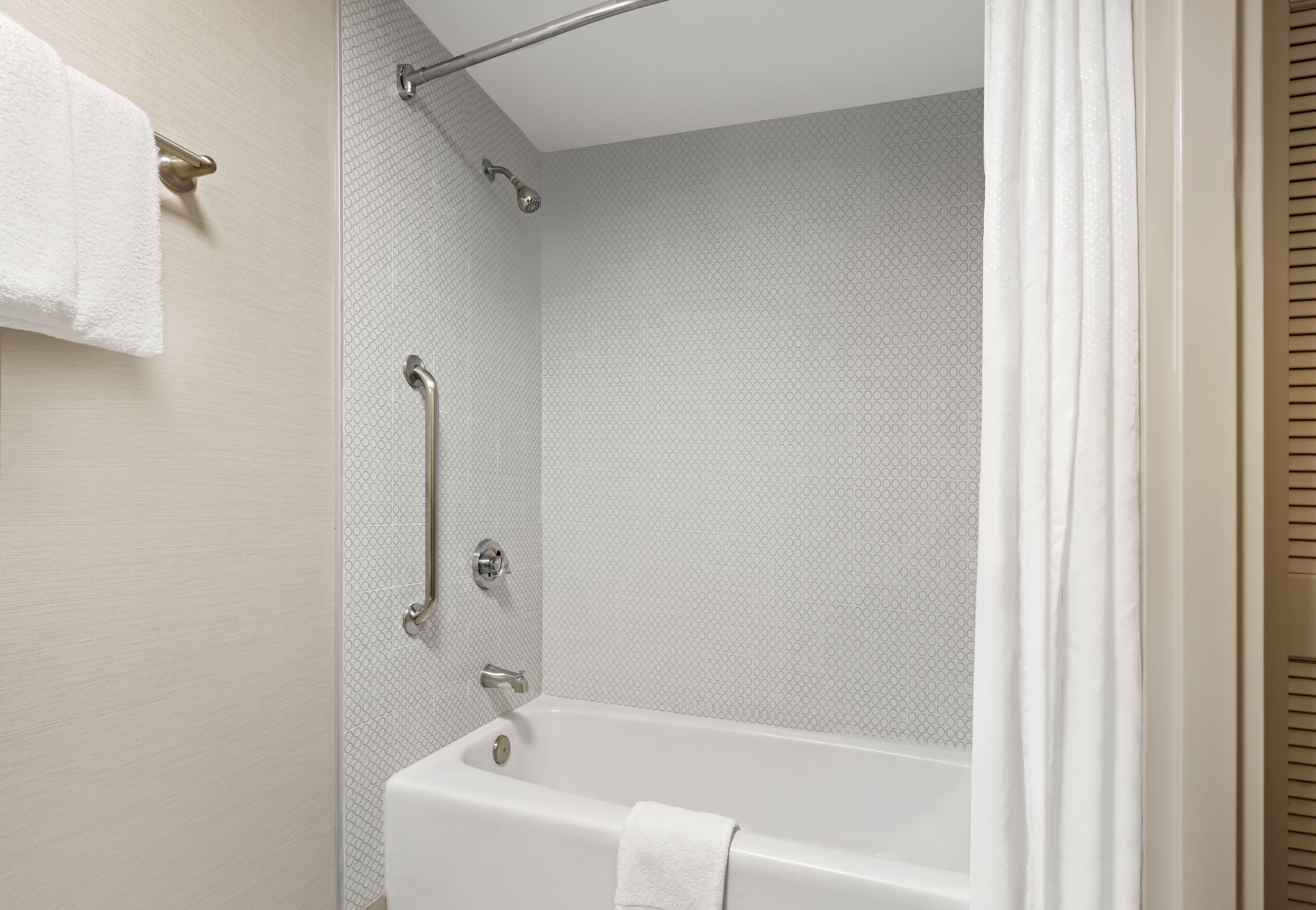 Un baño moderno con bañera, barras de apoyo y un perchero para toallas.
