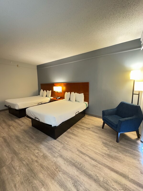 A hotel room with two beds, a chair, and a nightstand with a lamp.