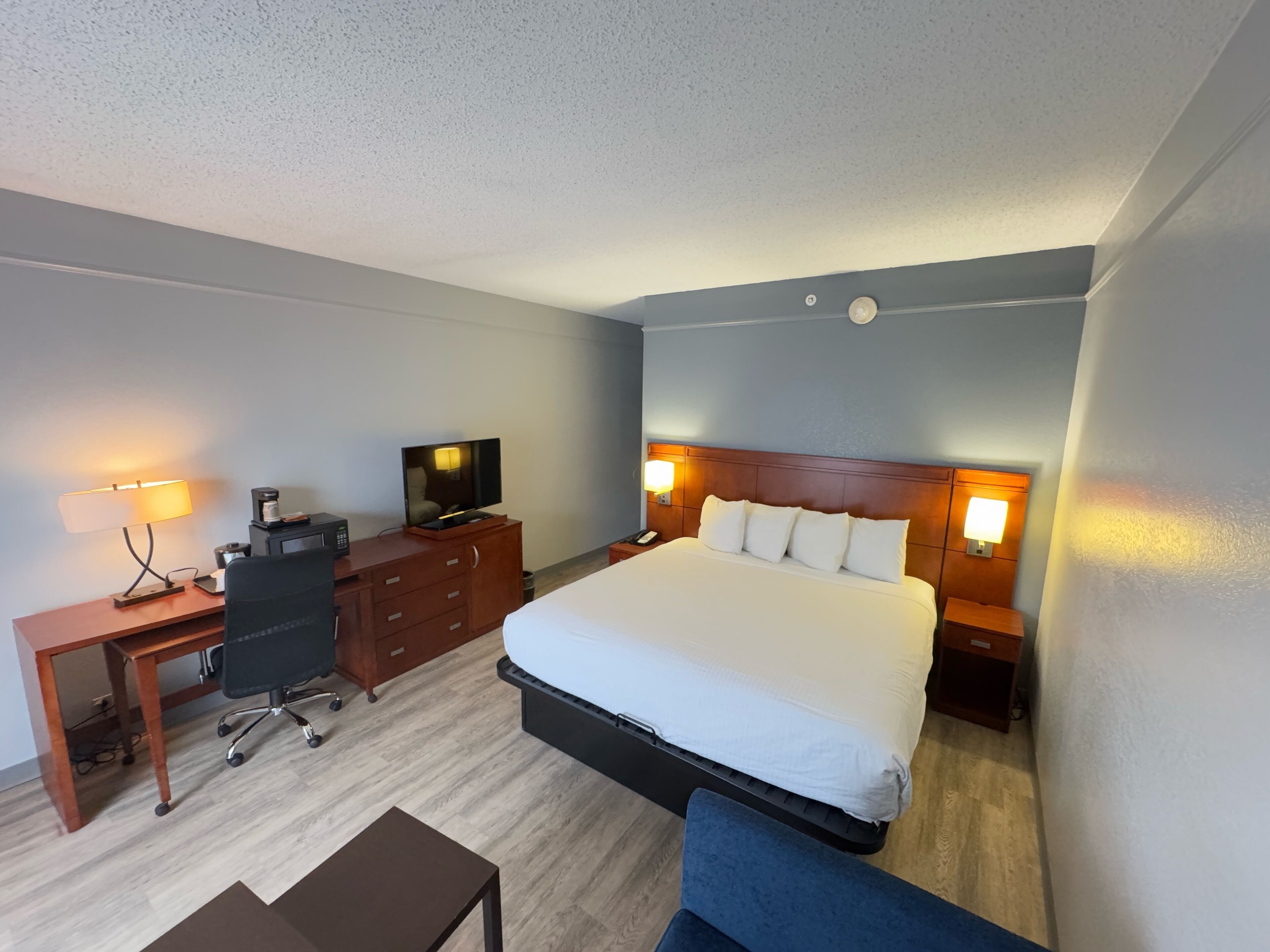 Une chambre d’hôtel équipée d’un lit, d’un bureau, d’une chaise, d’une télévision et de lampes de chevet.