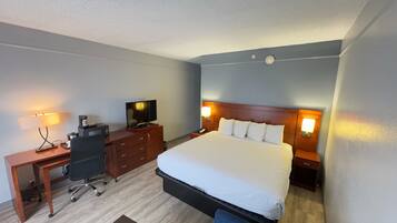 Une chambre d’hôtel équipée d’un lit, d’un bureau, d’une chaise, d’une télévision et de lampes de chevet.