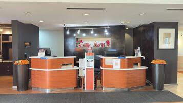A reception area with two wooden reception desks, a digital kiosk, and a wall-mounted security camera.