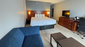 A hotel room with a large bed, bedside lamps, a television, a desk with a chair, and a blue sofa. - Super 8 by Wyndham Dallas Love Field Airport (Dallas)