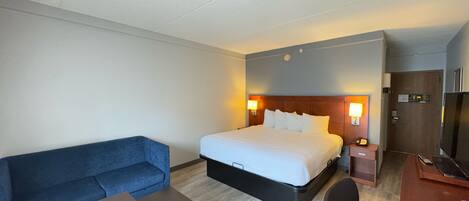 A hotel room with a bed, a blue sofa, a small table, a desk, and a TV.