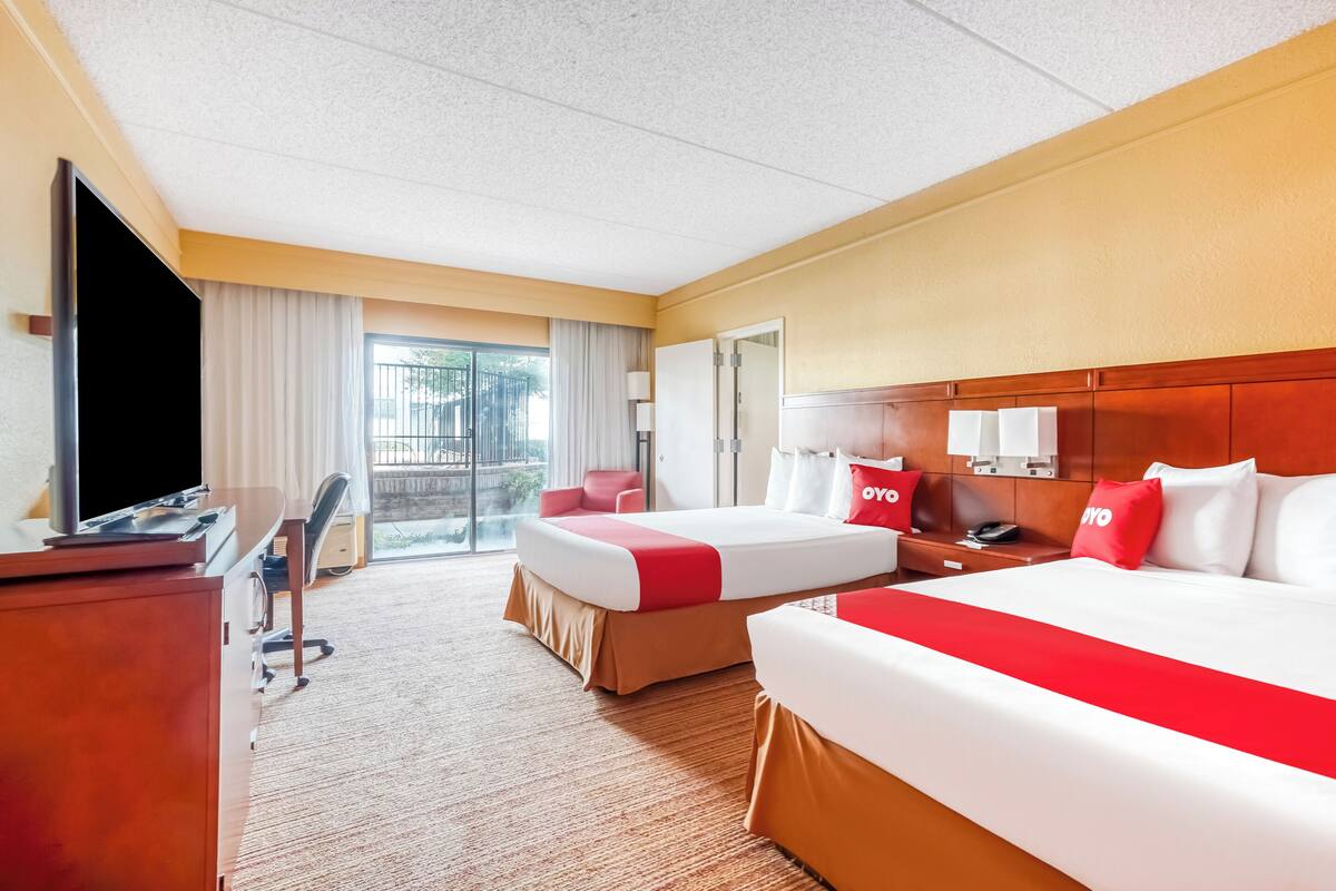 A hotel room with two beds, a desk, a TV, a chair, a lamp, and a window with curtains.