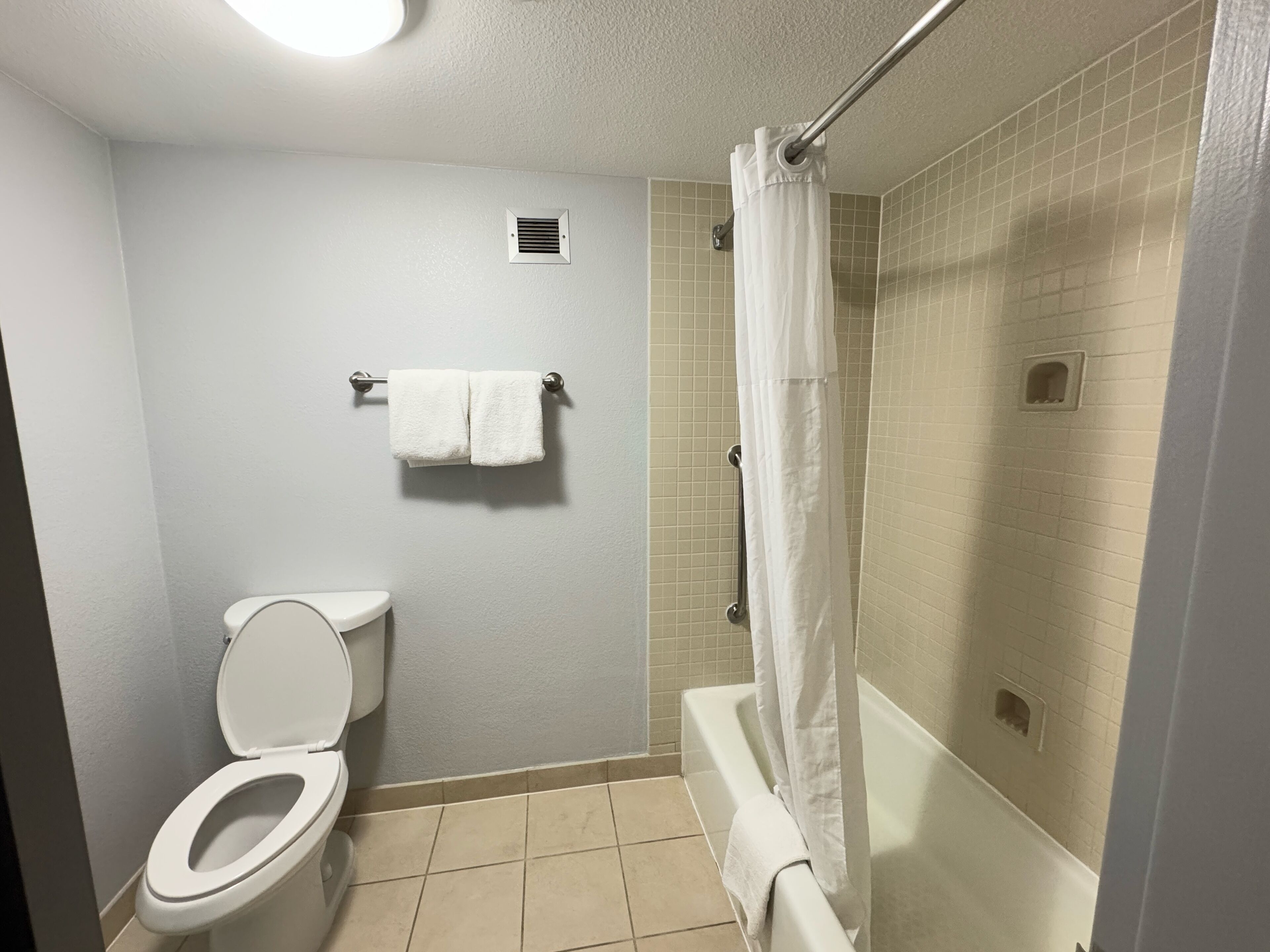 A bathroom with a toilet, a shower with a curtain, and a towel rack with two towels.