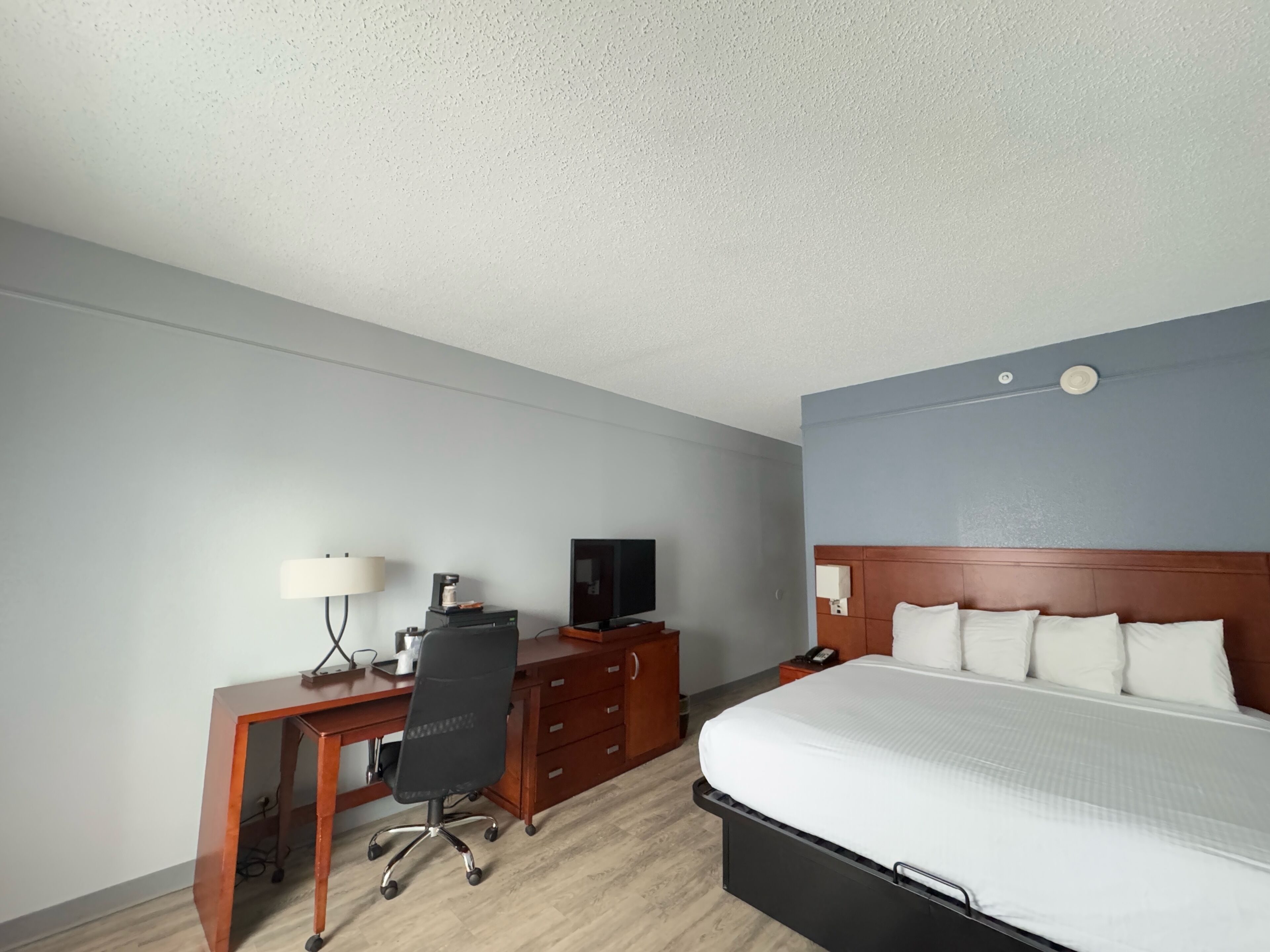 Ein Hotelzimmer mit einem Bett, einem Schreibtisch mit Stuhl, einem Fernseher und einer Lampe.