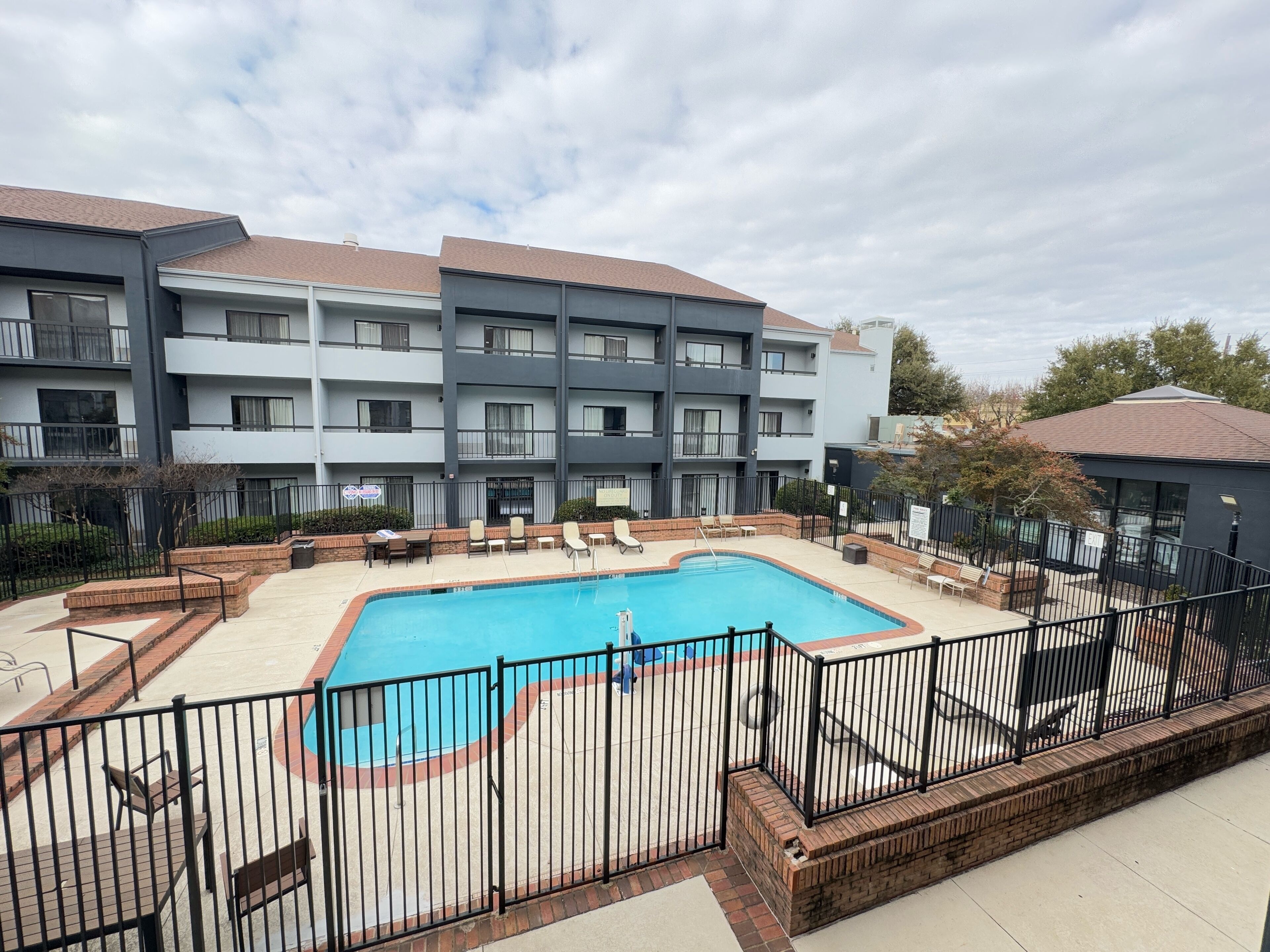 A modern multi-story building with a swimming pool surrounded by lounge chairs and a fenced patio area.