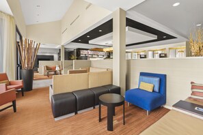 A modern hotel lobby with a seating area, a reception desk, and a view into the dining area.