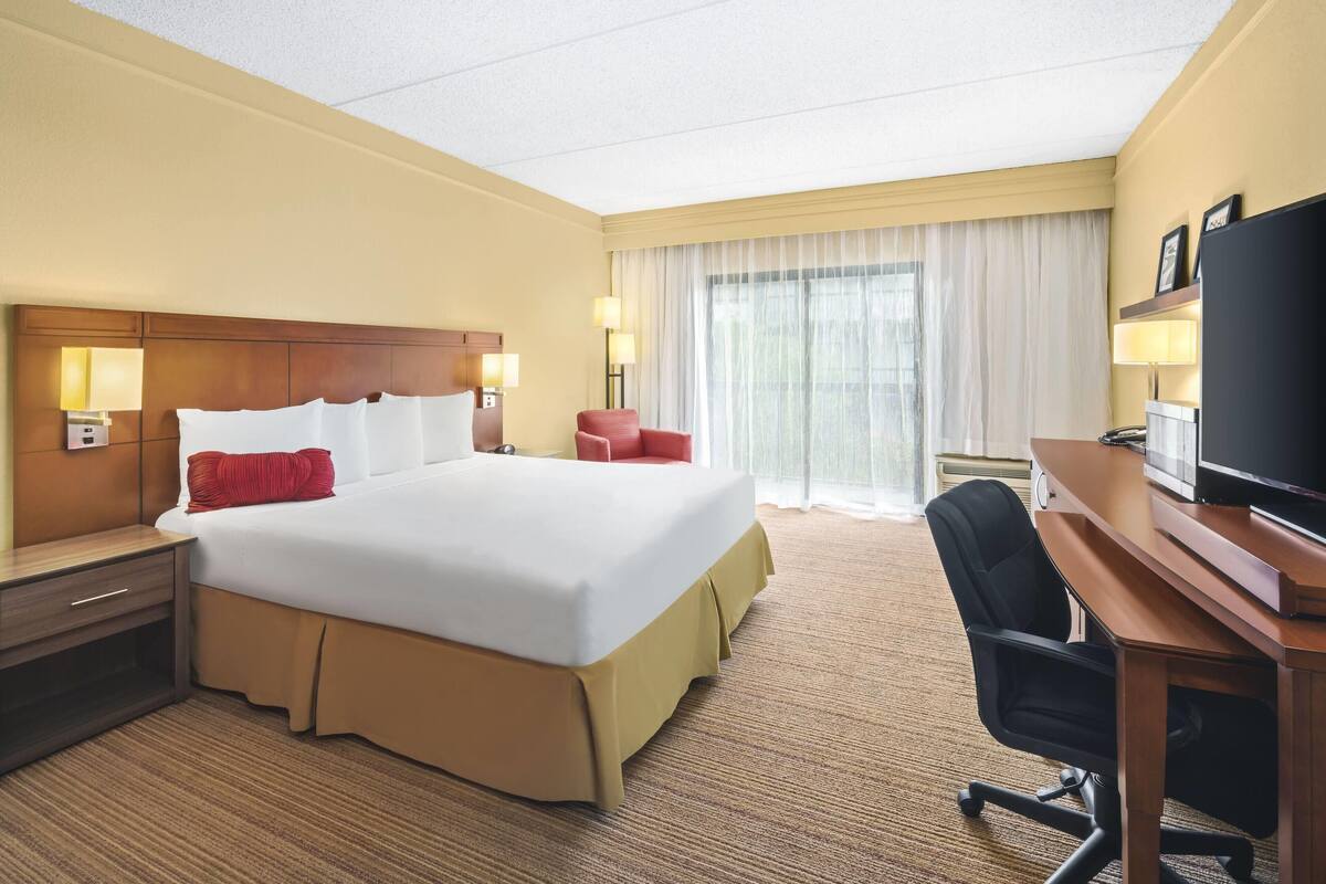 A hotel room with a large bed, a desk with a chair, a television, and a window with curtains.