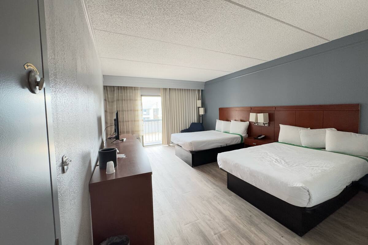 A hotel room with two beds, a desk, a chair, a TV, and a window with curtains.