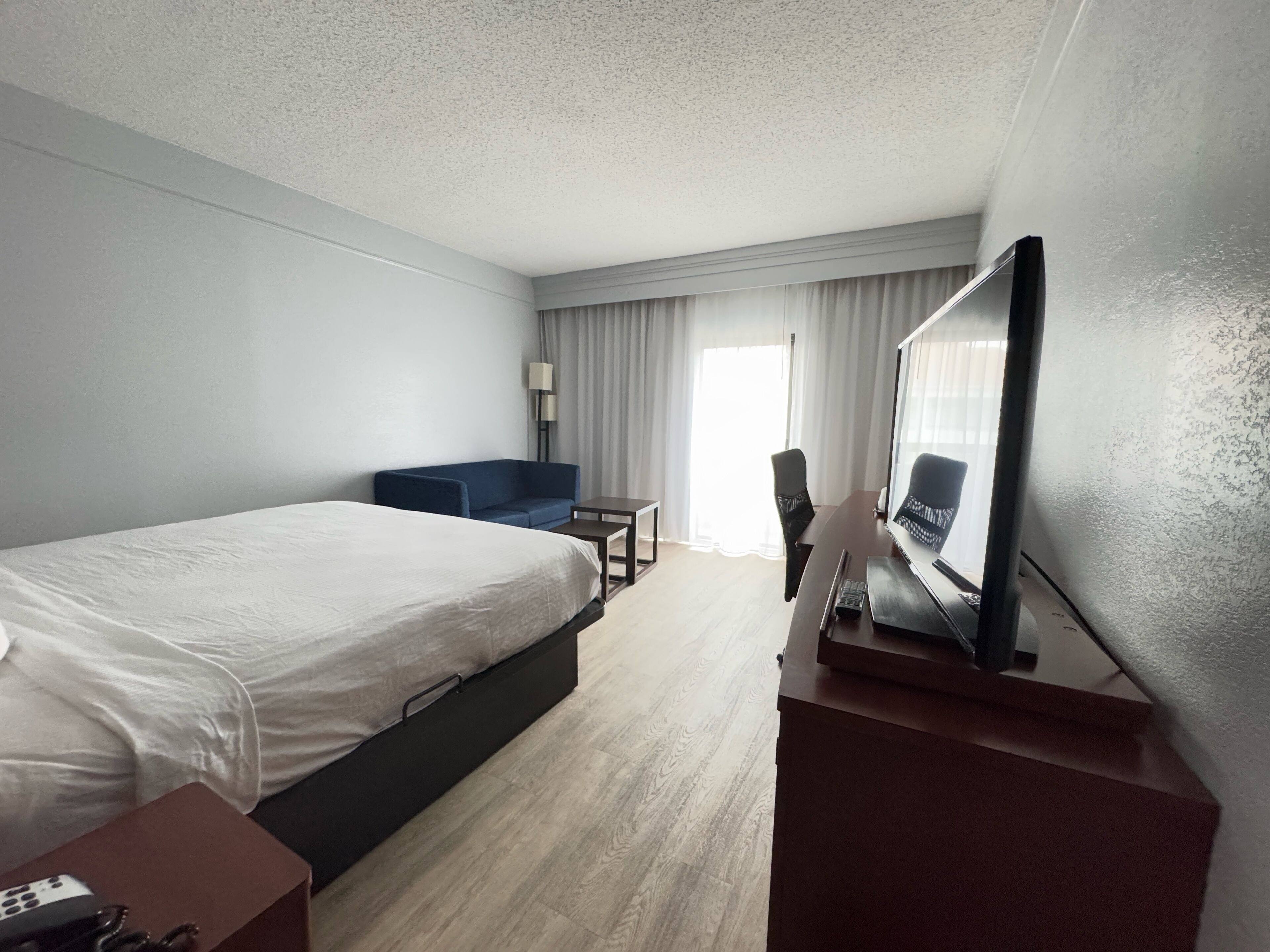 Una habitación de hotel con una cama grande, un escritorio, una silla, un televisor y una ventana con cortinas.