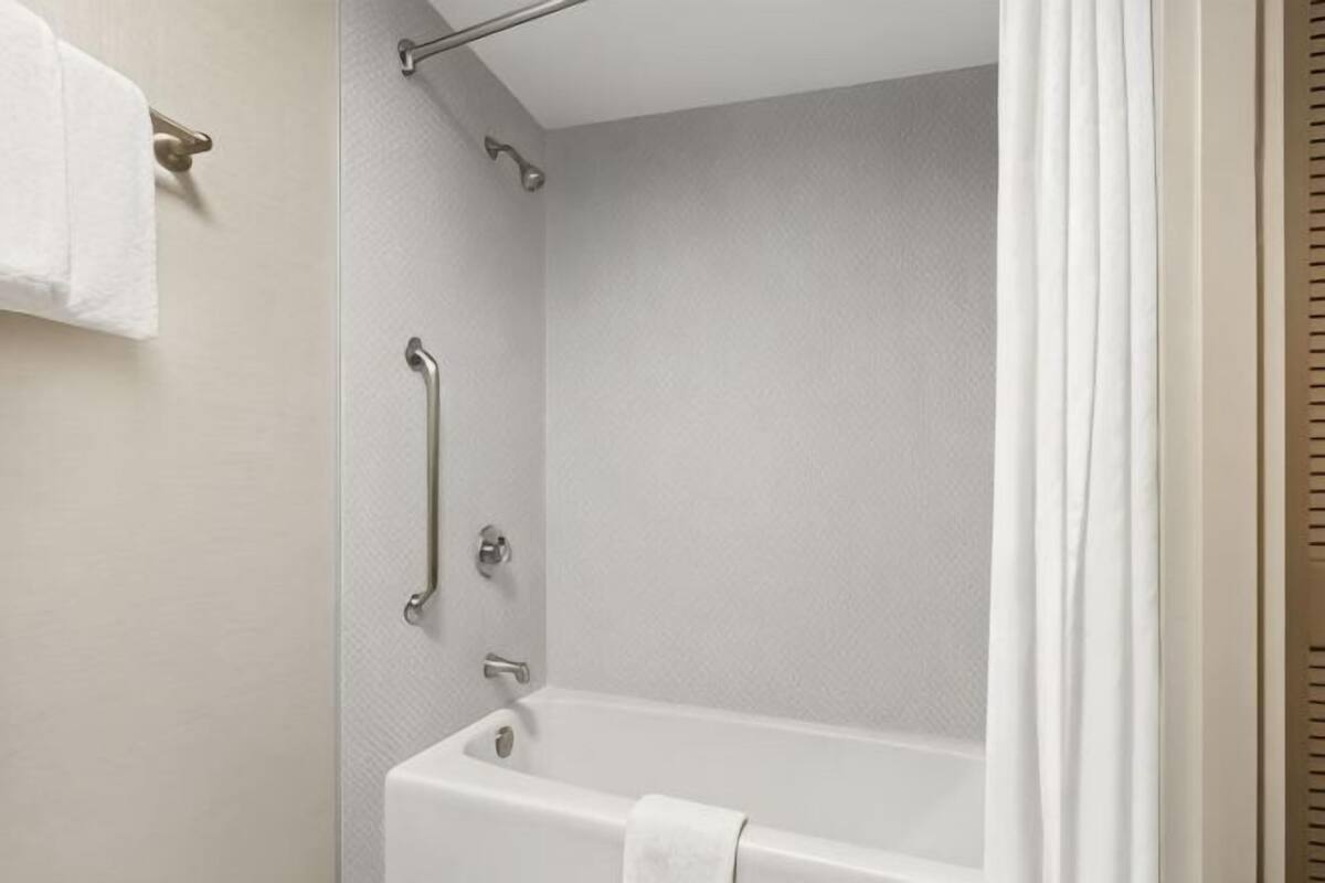 A bathroom with a bathtub, grab bars, and a towel rack.