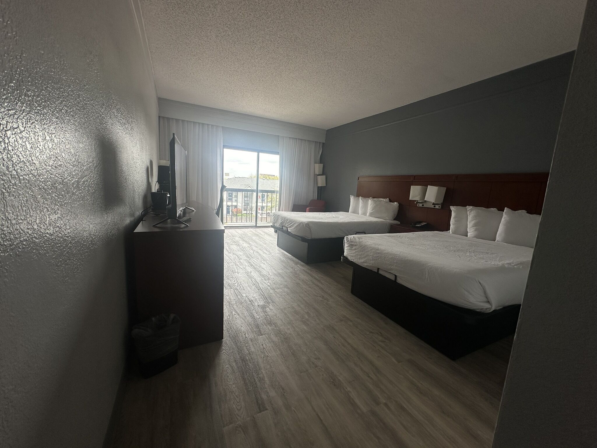 Ein Hotelzimmer mit zwei Betten, einem Schreibtisch, einem Stuhl und einem großen Fenster.