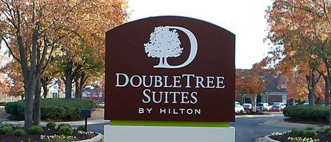 A sign for DoubleTree Suites by Hilton, surrounded by landscaped gardens and autumn-colored trees.