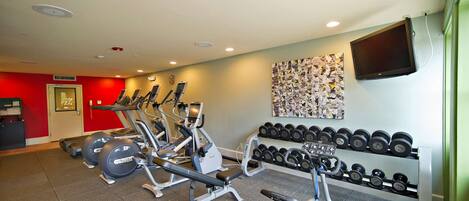 A gym with exercise equipment, a wall-mounted TV, and a rack of dumbbells.