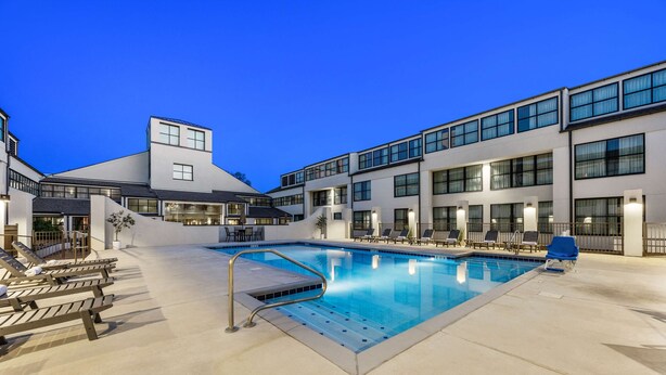 A modern building with a swimming pool, lounge chairs, and a covered seating area.
