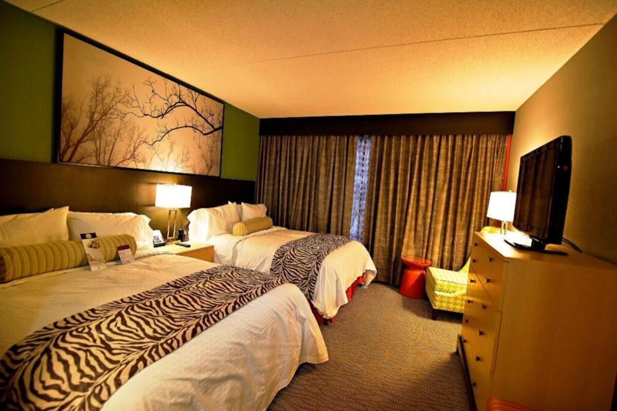 Een hotelkamer met twee bedden, een groot schilderij aan de muur, een bureau met een lamp en een dressoir.