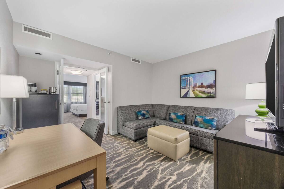 Een moderne hotelkamer met een zithoek, een bank, een televisie en een schilderij aan de muur.