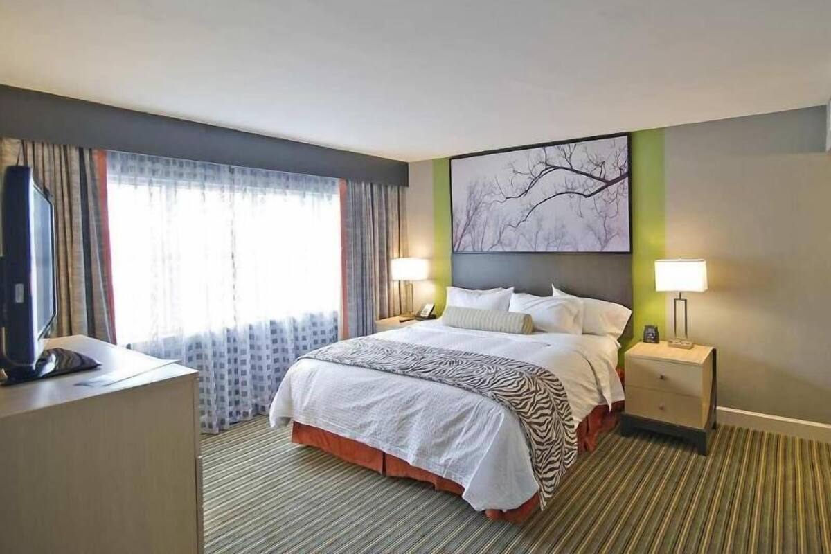 Een hotelkamer met een bed, twee nachtkastjes, een bureau, een televisie en een raam met gordijnen.