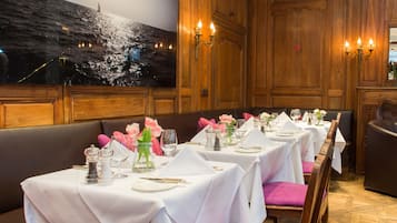 A dining area with tables set for service, wooden paneling, and a large painting of a seascape on the wall.