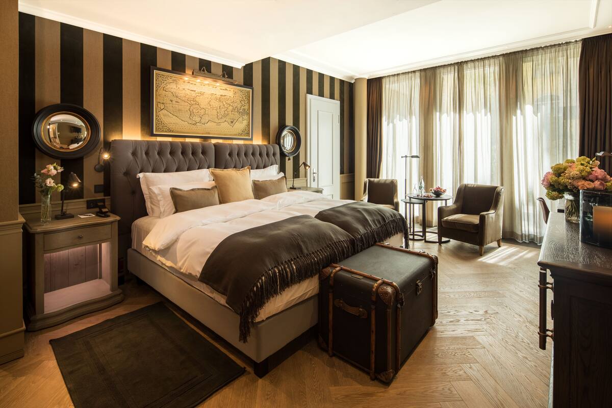 Habitación de hotel con una cama grande, un mapa en la pared, un escritorio con una lámpara y una silla.