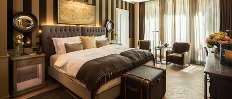 A hotel room with a large bed, a map on the wall, a desk with a lamp, and a chair.