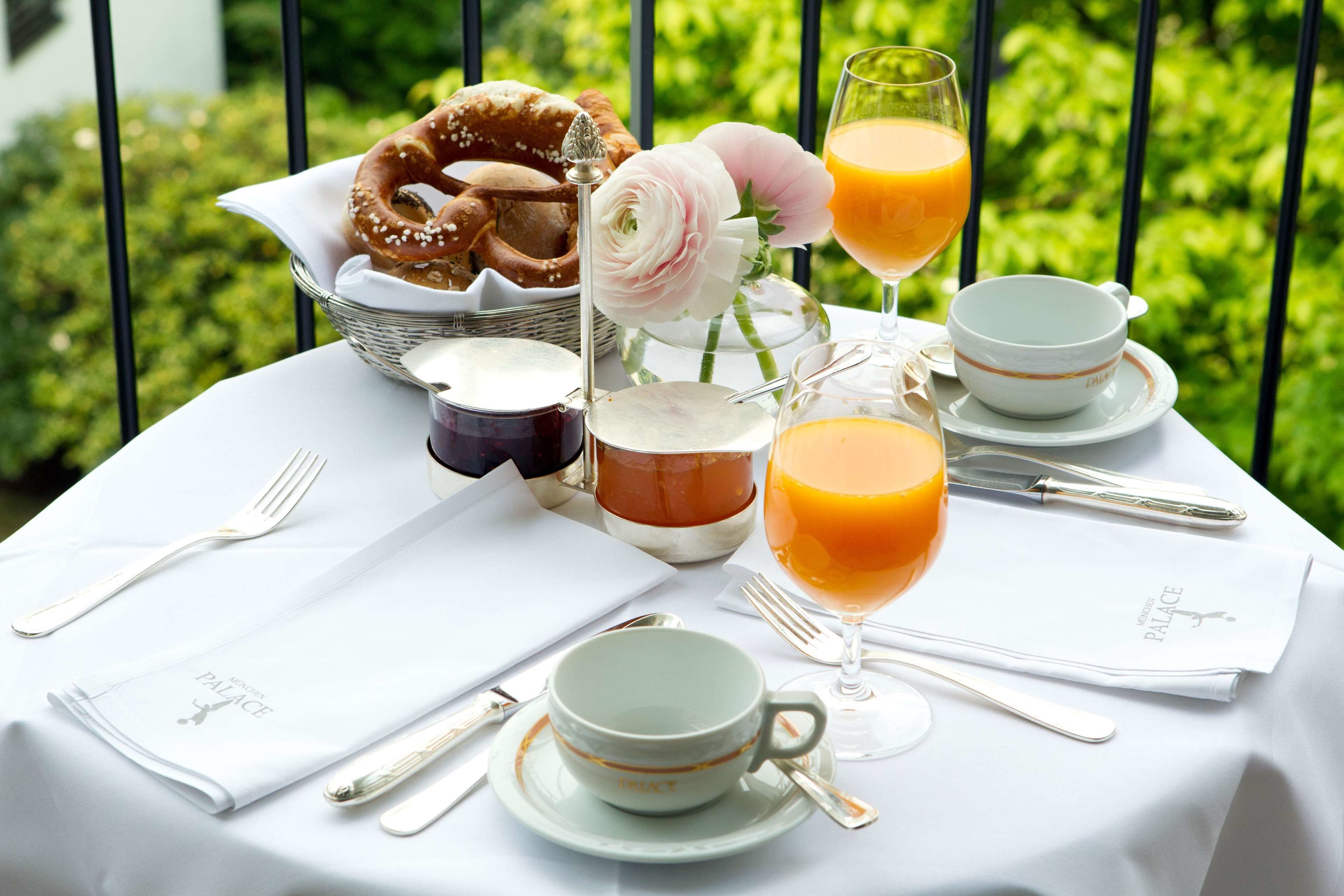 A breakfast setting with a table set for two, including plates, cups, a glass of orange juice, a pastry, and a flower arrangement.