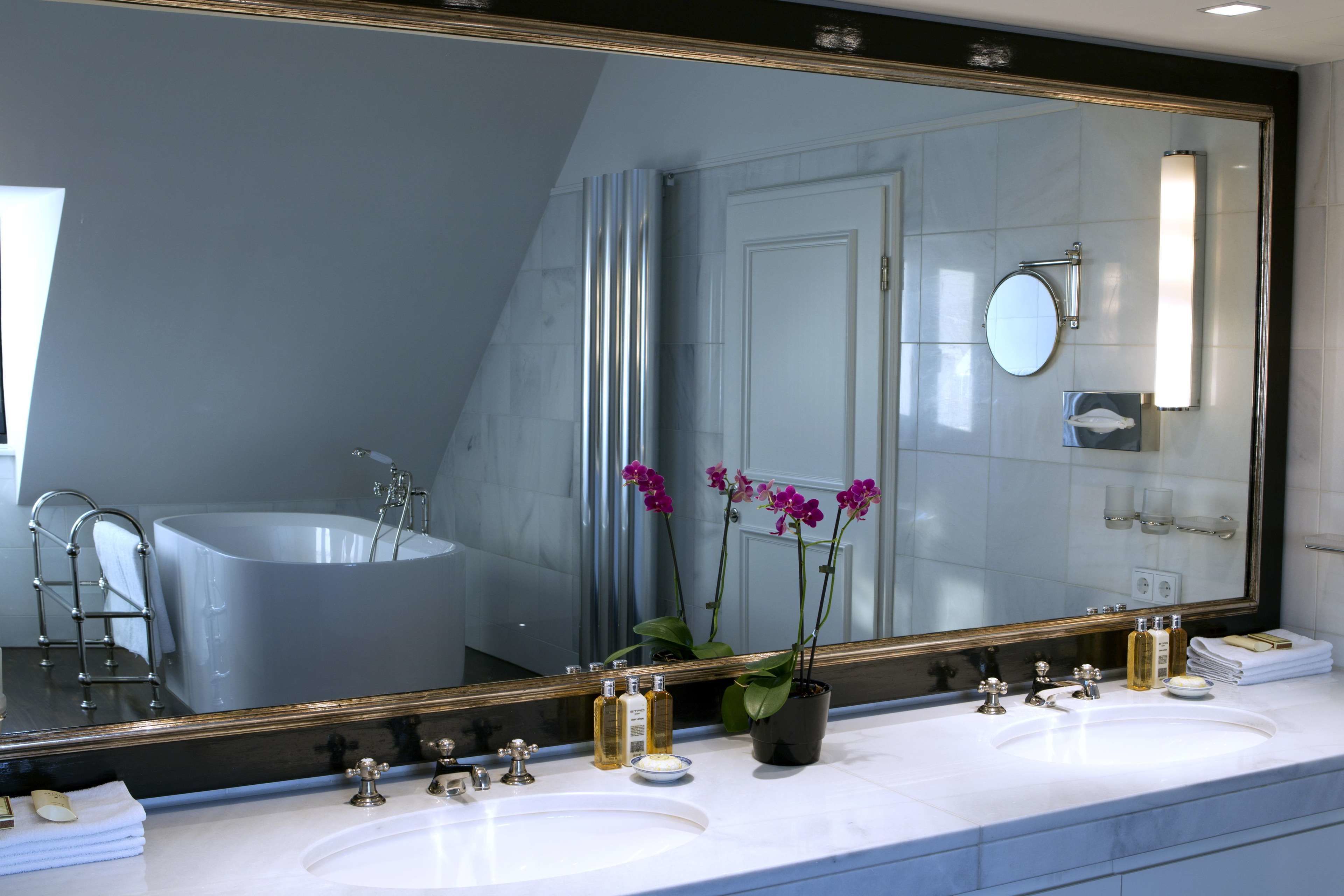 A modern bathroom with two sinks, a large mirror, and a bathtub.