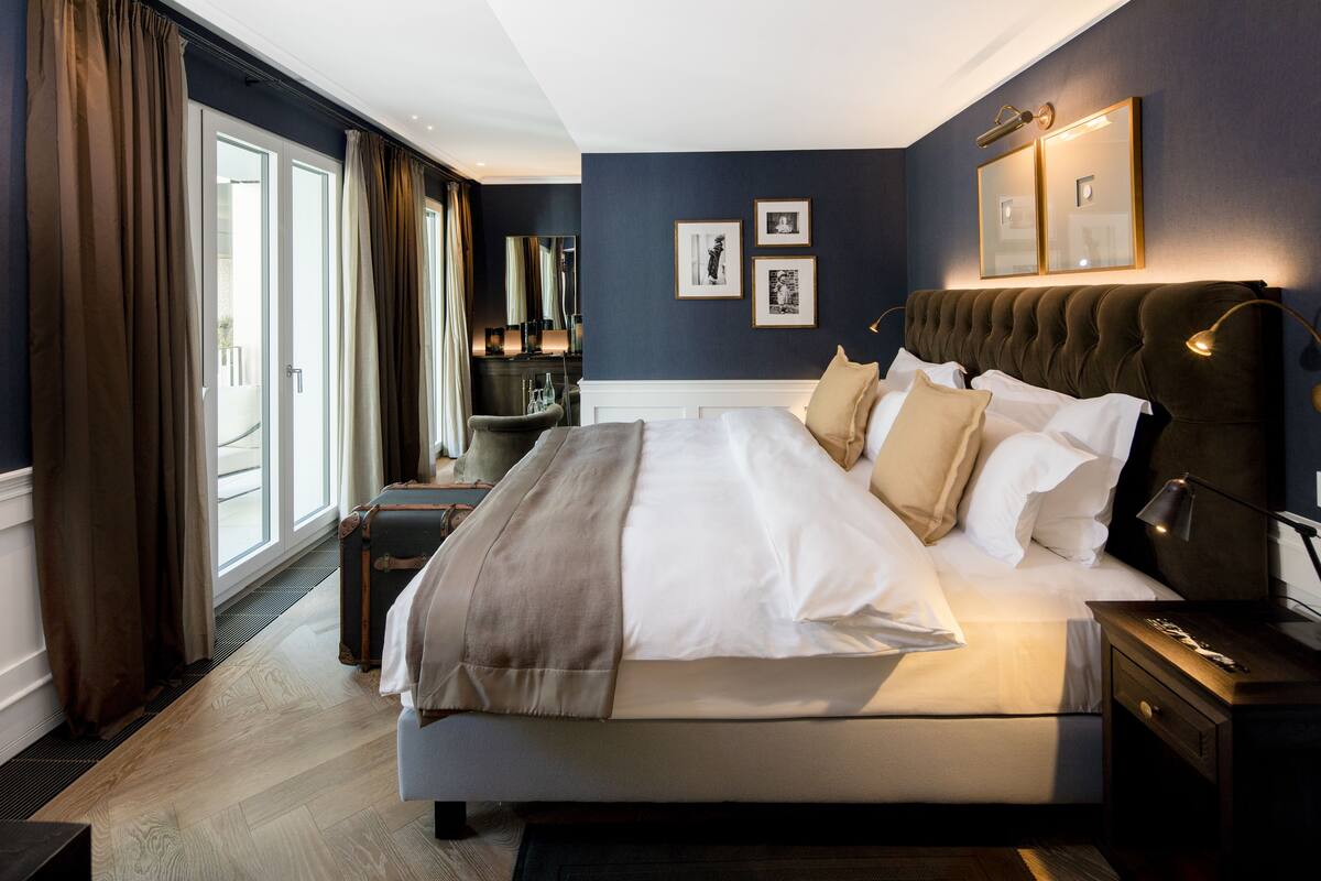 Un dormitorio moderno de hotel con una cama grande, una mesita de noche, una lámpara y vistas al exterior.