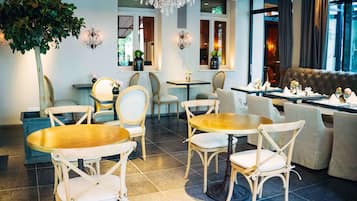 Un comedor con mesas y sillas redondas, una araña y un ventanal con cortinas.