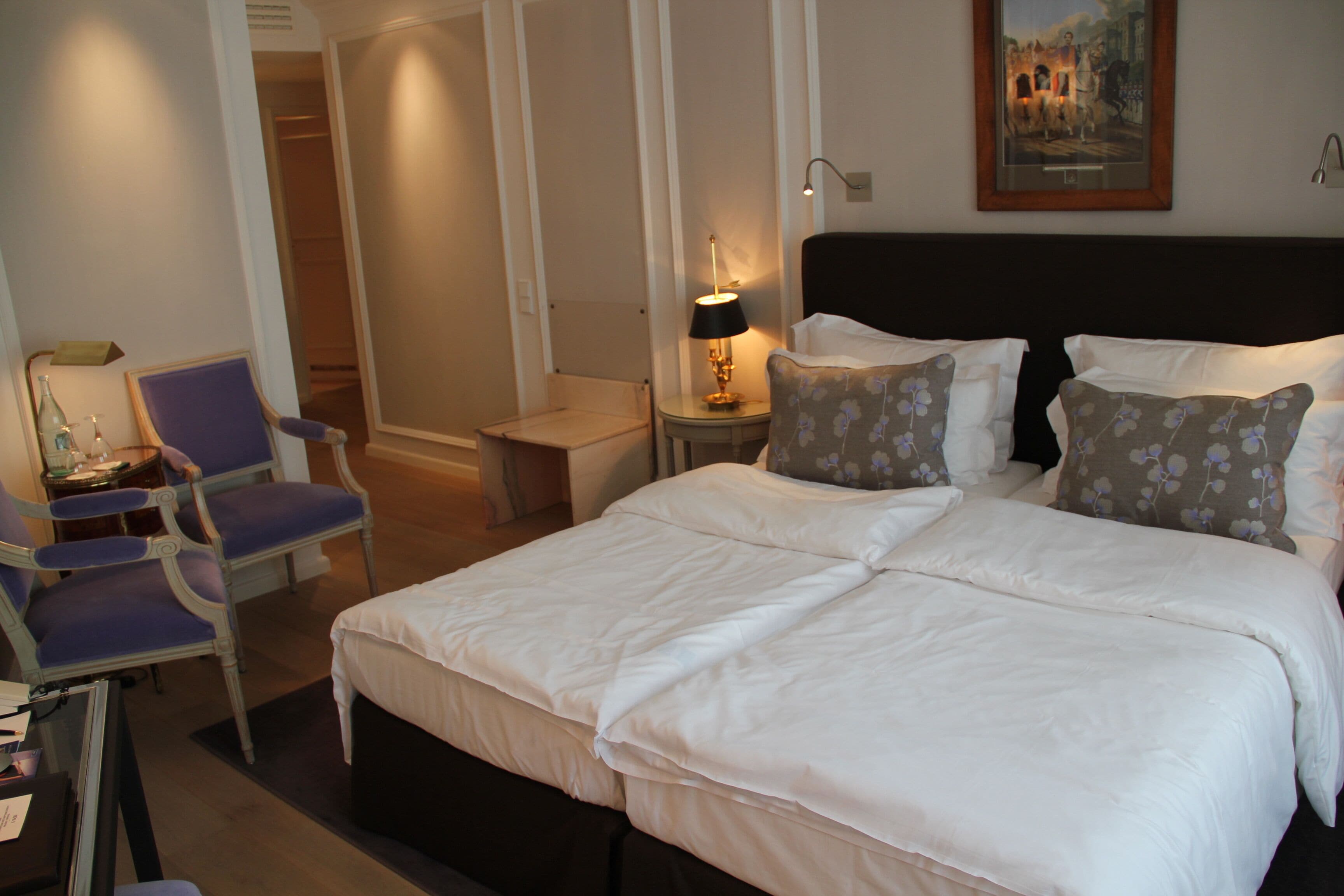 A hotel room with a large bed, two chairs, a small table, and a painting on the wall.