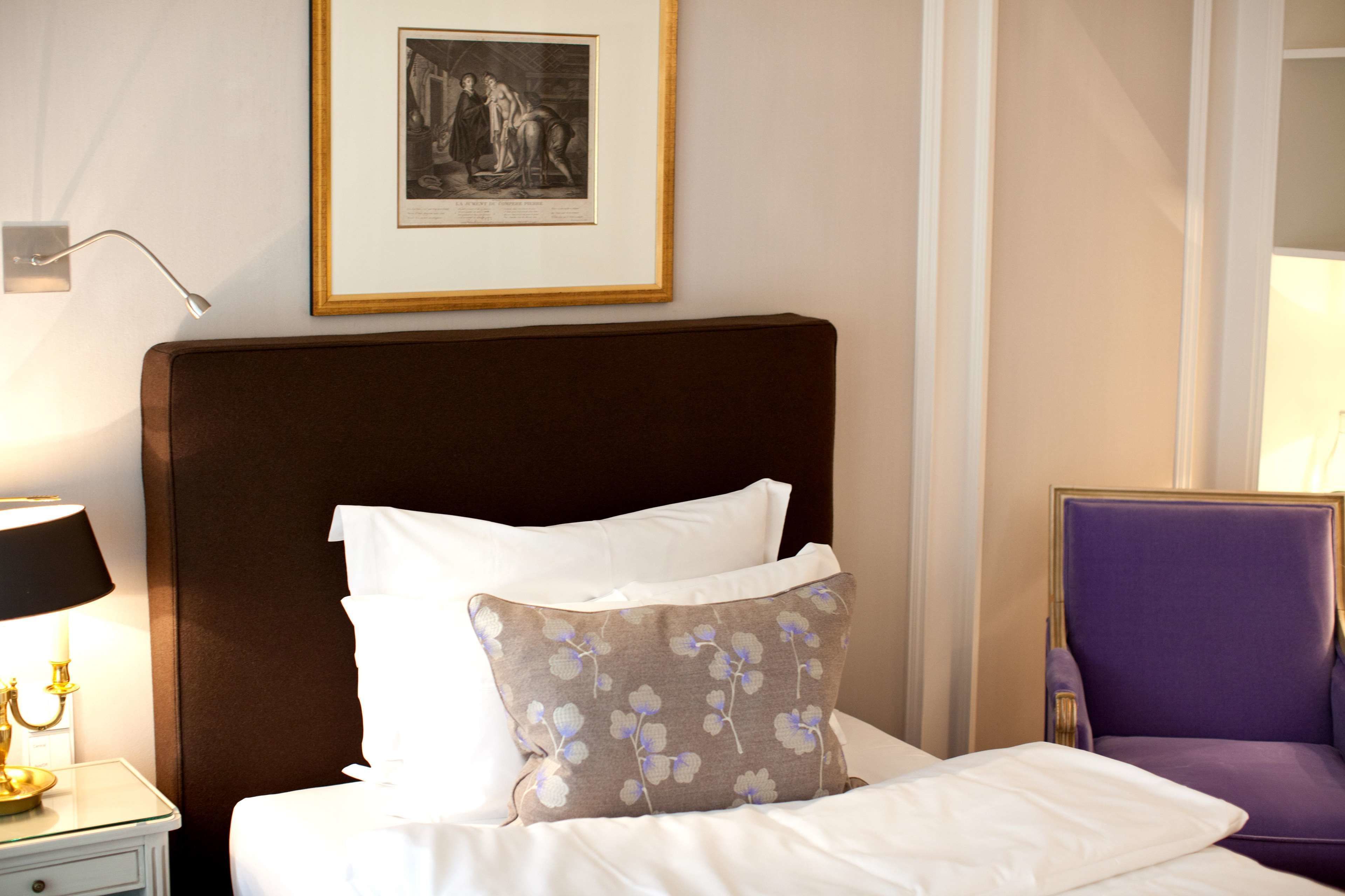 A neatly made bed with a brown headboard, white pillows, and a floral-patterned pillow. A framed black and white artwork hangs above the bed.
