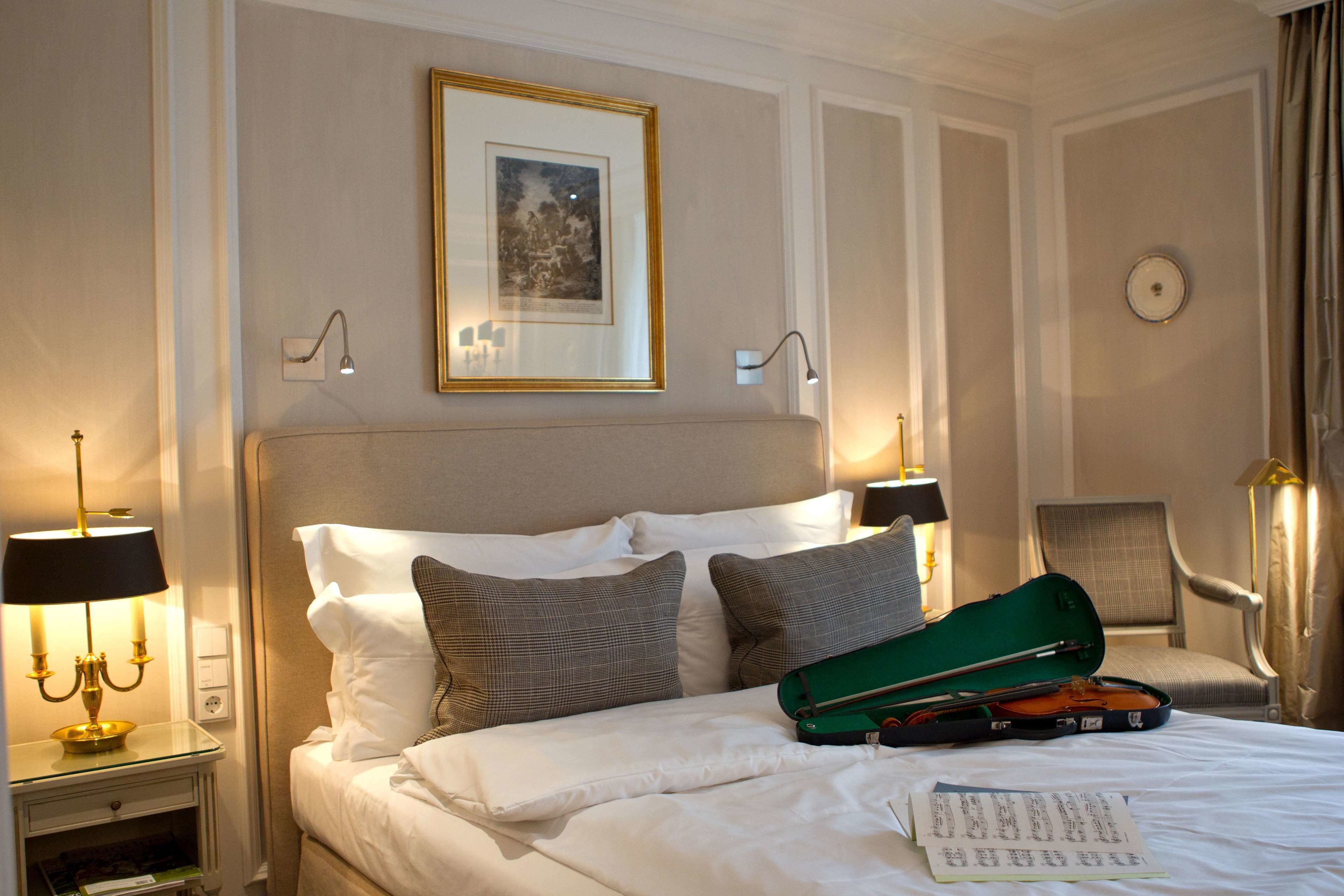 A hotel room with a neatly made bed, a green violin case, and a framed picture on the wall.