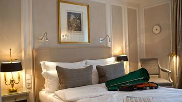 A hotel room with a neatly made bed, a green violin case, and a framed picture on the wall.