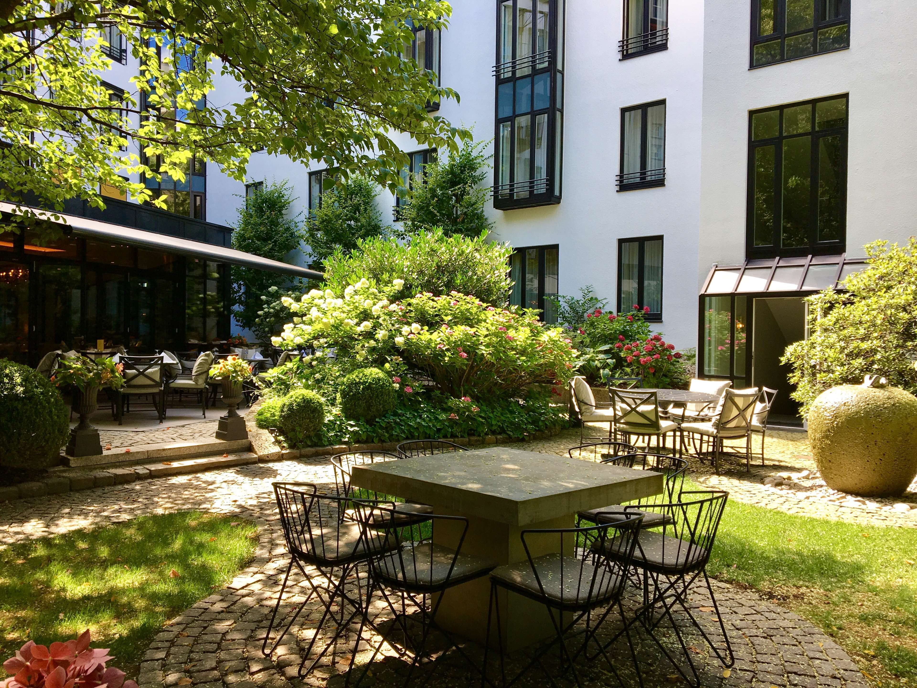 An outdoor seating area with a stone table and chairs, surrounded by lush greenery and flowering plants.