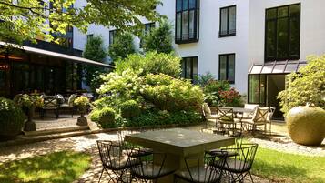 An outdoor seating area with a stone table and chairs, surrounded by lush greenery and flowering plants.