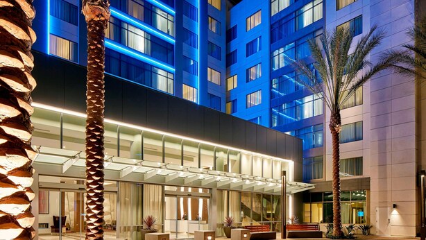 A modern hotel with a glass facade, outdoor seating area, and palm trees. - Residence Inn by Marriott at Anaheim Resort/Convention Cntr (Anaheim)