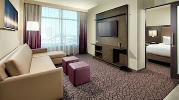 Habitación de hotel con sofá, reposapiés, televisor y cama.
