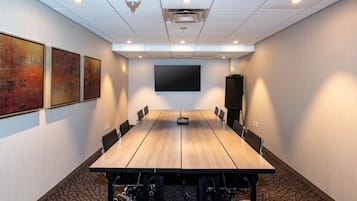 Une salle de conférence équipée d’une longue table, de chaises, d’un projecteur et d’un grand écran.
