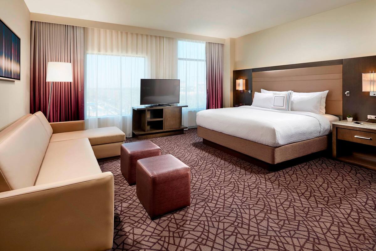 A hotel room with a large bed, a sofa, a TV, and a desk.