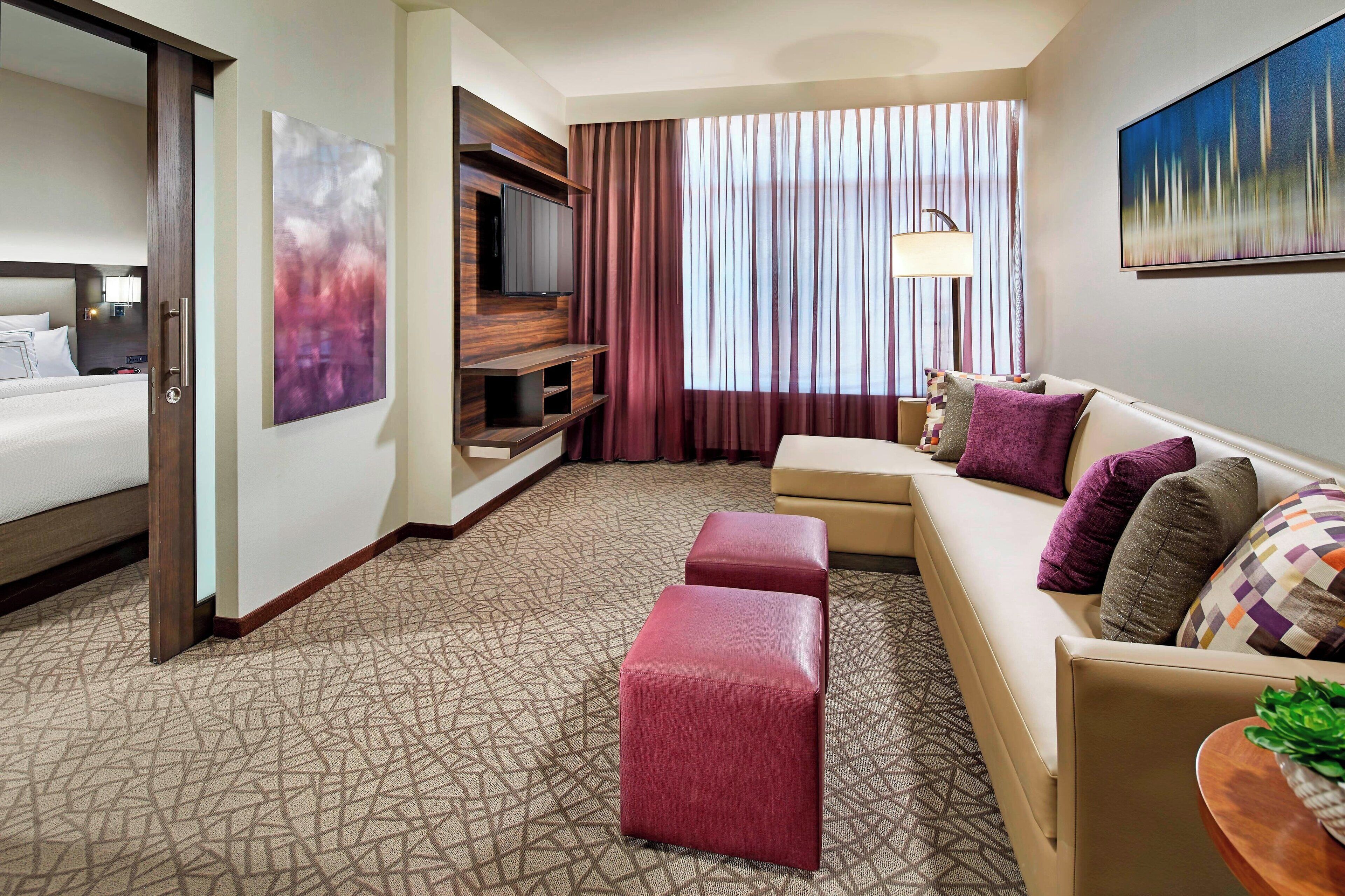A hotel room with a bed, a sofa, a TV, a lamp, and a painting on the wall.