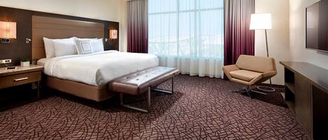 Ein Hotelzimmer mit einem großen Bett, einer Bank, einem Sessel, einem Schreibtisch und einem Fernseher.